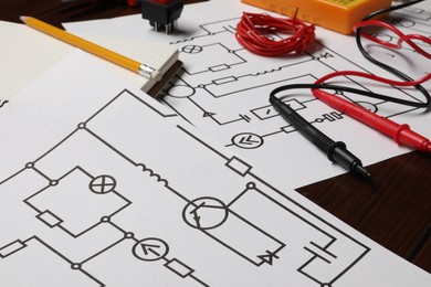 Photo of Wiring diagrams and different electrician's equipment on wooden table, closeup