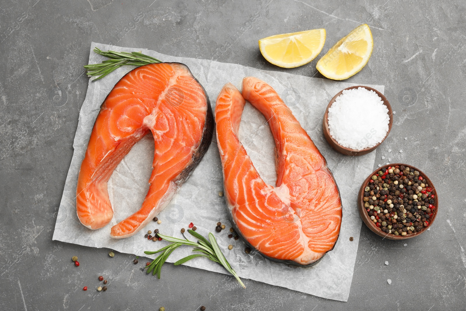 Photo of Fresh salmon steaks with spices, lemon and rosemary on grey table, flat lay