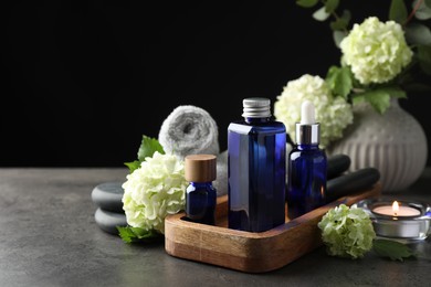 Photo of Spa composition. Cosmetic products, burning candle and hydrangea flowers on gray table against black background, space for text