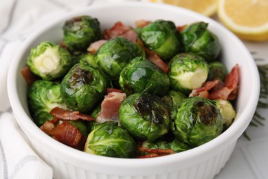 Delicious roasted Brussels sprouts and bacon in bowl on table, closeup