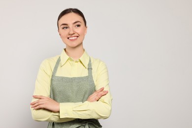 Beautiful young woman in clean apron with pattern on light grey background. Space for text