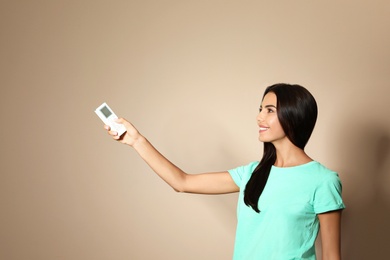 Young woman with air conditioner remote on beige background. Space for text