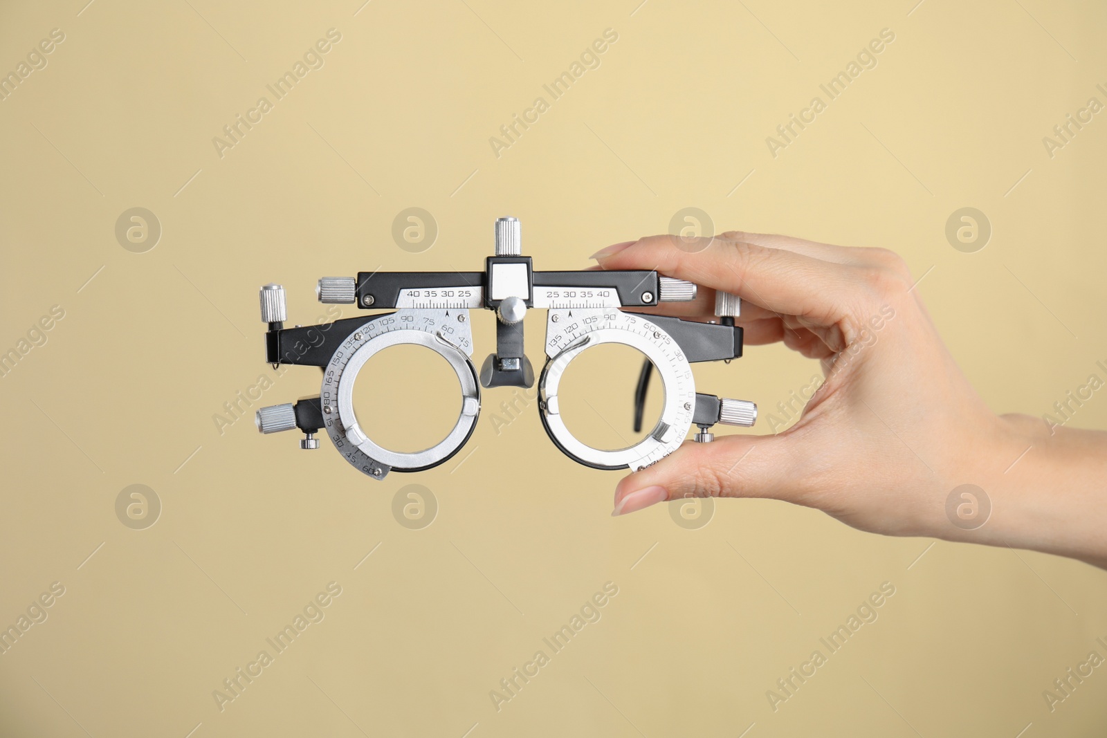 Photo of Woman holding trial frame on beige background, closeup. Ophthalmologist tool