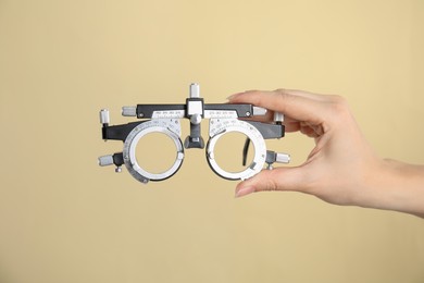 Photo of Woman holding trial frame on beige background, closeup. Ophthalmologist tool