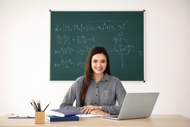 Young female teacher working at table in classroom