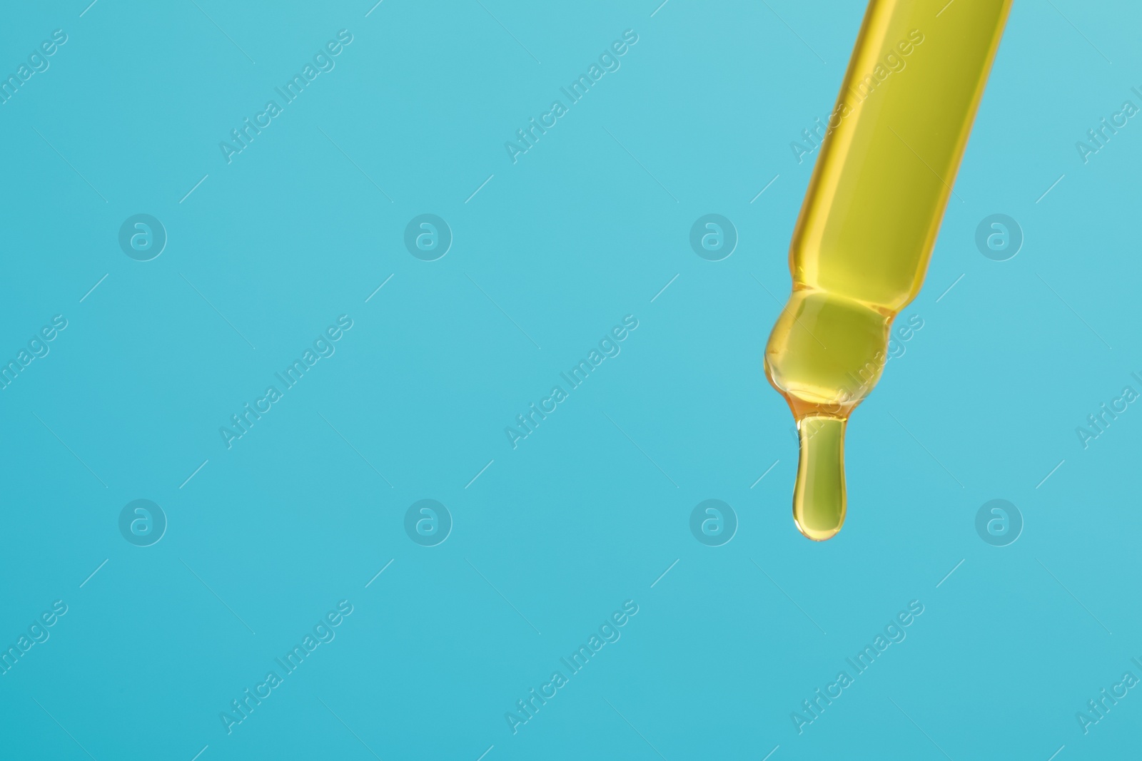 Photo of Dripping yellow serum from pipette on light blue background, closeup. Space for text