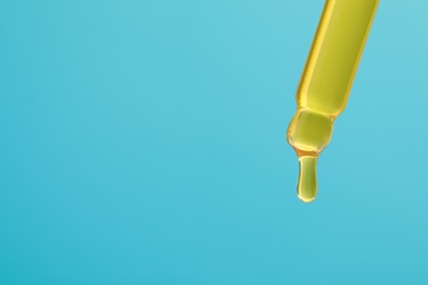 Photo of Dripping yellow serum from pipette on light blue background, closeup. Space for text