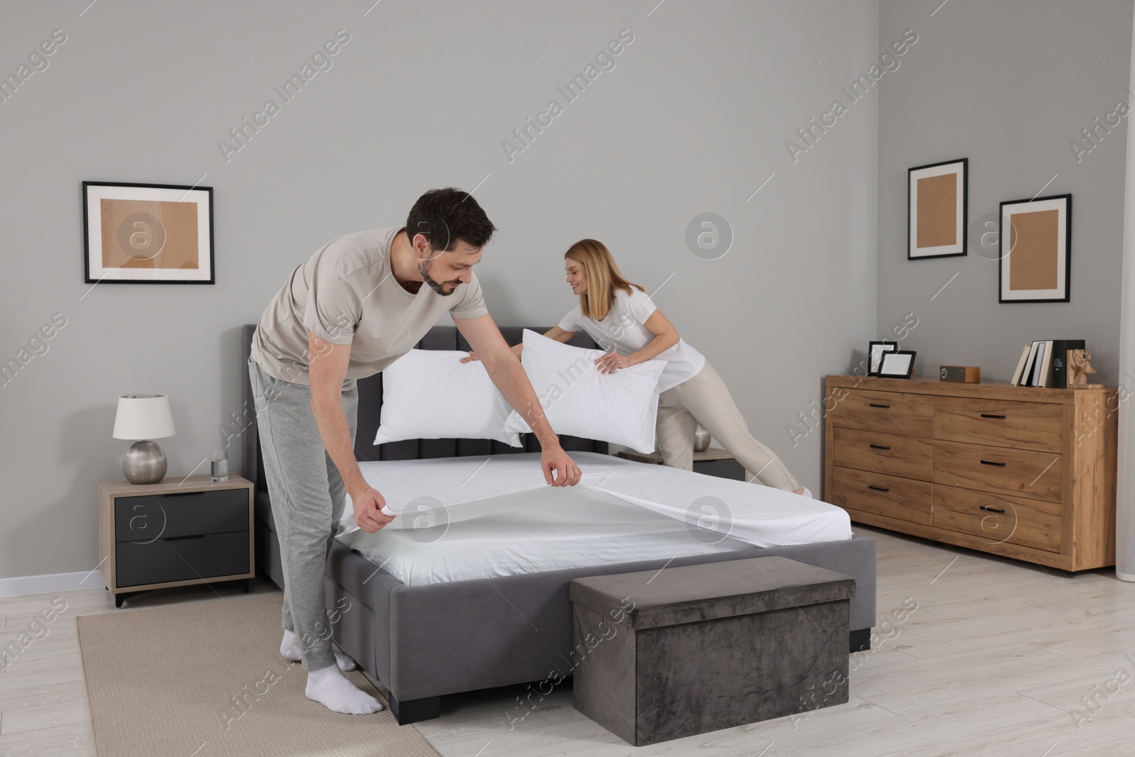 Photo of Couple changing bed linens in room. Domestic chores