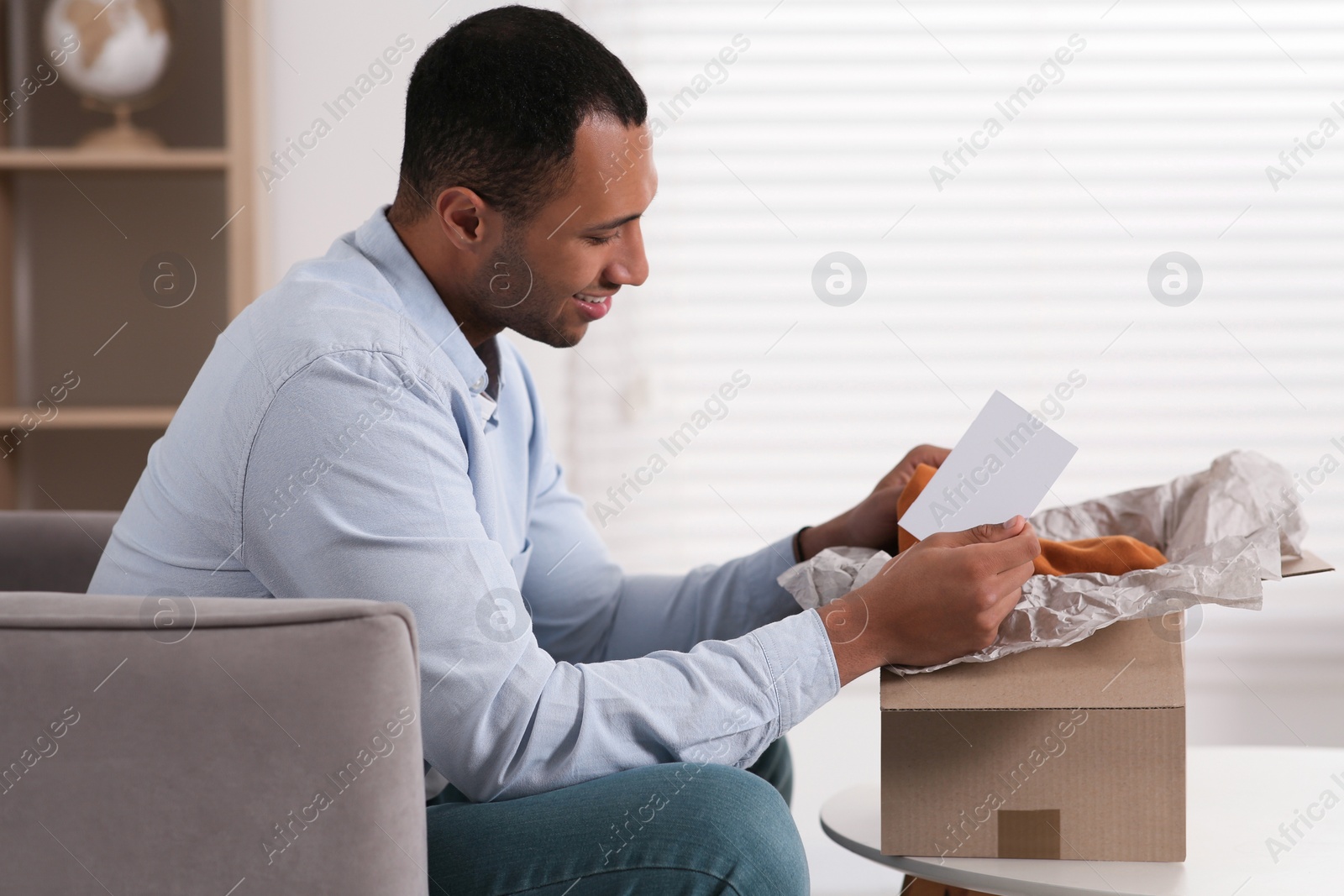 Photo of Happy man with greeting card near parcel at home. Internet shopping