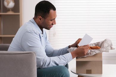 Photo of Happy man with greeting card near parcel at home. Internet shopping