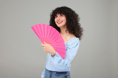 Happy woman holding hand fan on light grey background