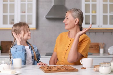 Photo of Happy grandmother giving high five to her granddaughter in kitchen