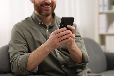 Smiling man using smartphone on sofa at home, closeup