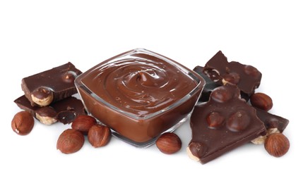 Photo of Chocolate pieces, bowl of sweet paste and hazelnuts on white background
