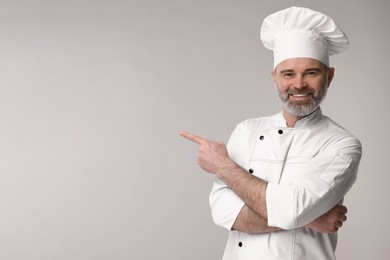 Photo of Happy chef in uniform pointing at something on grey background, space for text