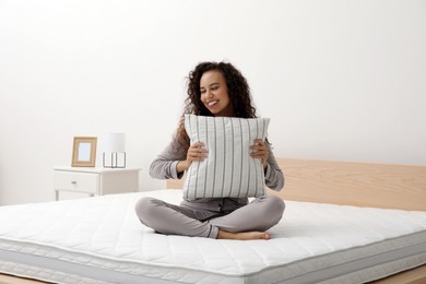 Photo of Happy young African American woman hugging pillow on bed with comfortable mattress at home