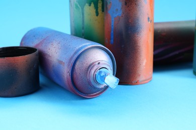 Photo of Spray paint cans and caps on light blue background, closeup