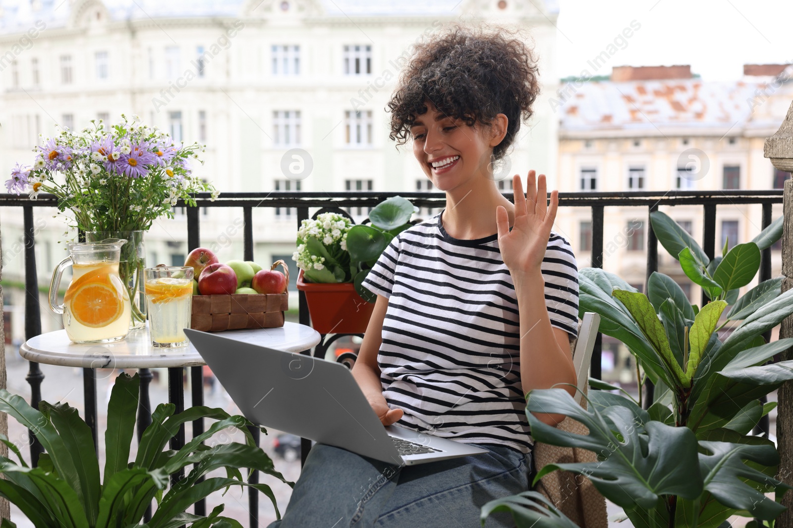 Photo of Beautiful young woman using laptop on balcony with green houseplants