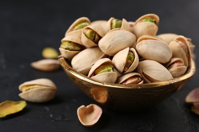 Tasty pistachios in bowl on black table, closeup