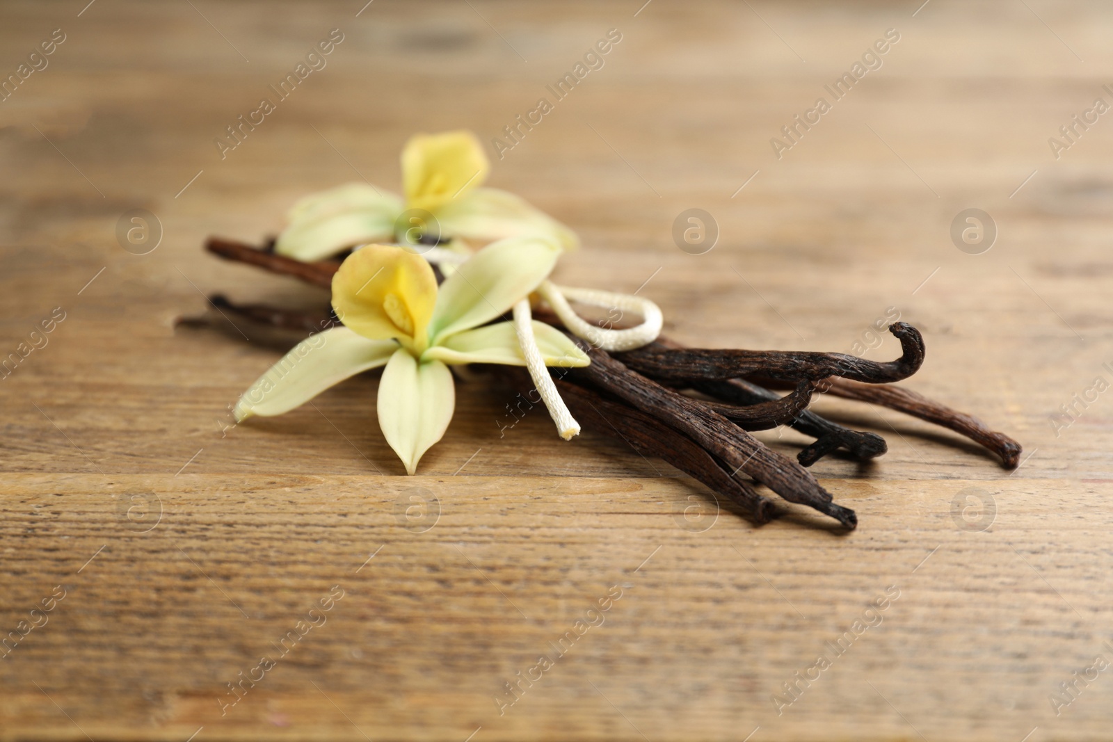 Photo of Aromatic vanilla sticks and flowers on wooden table, closeup