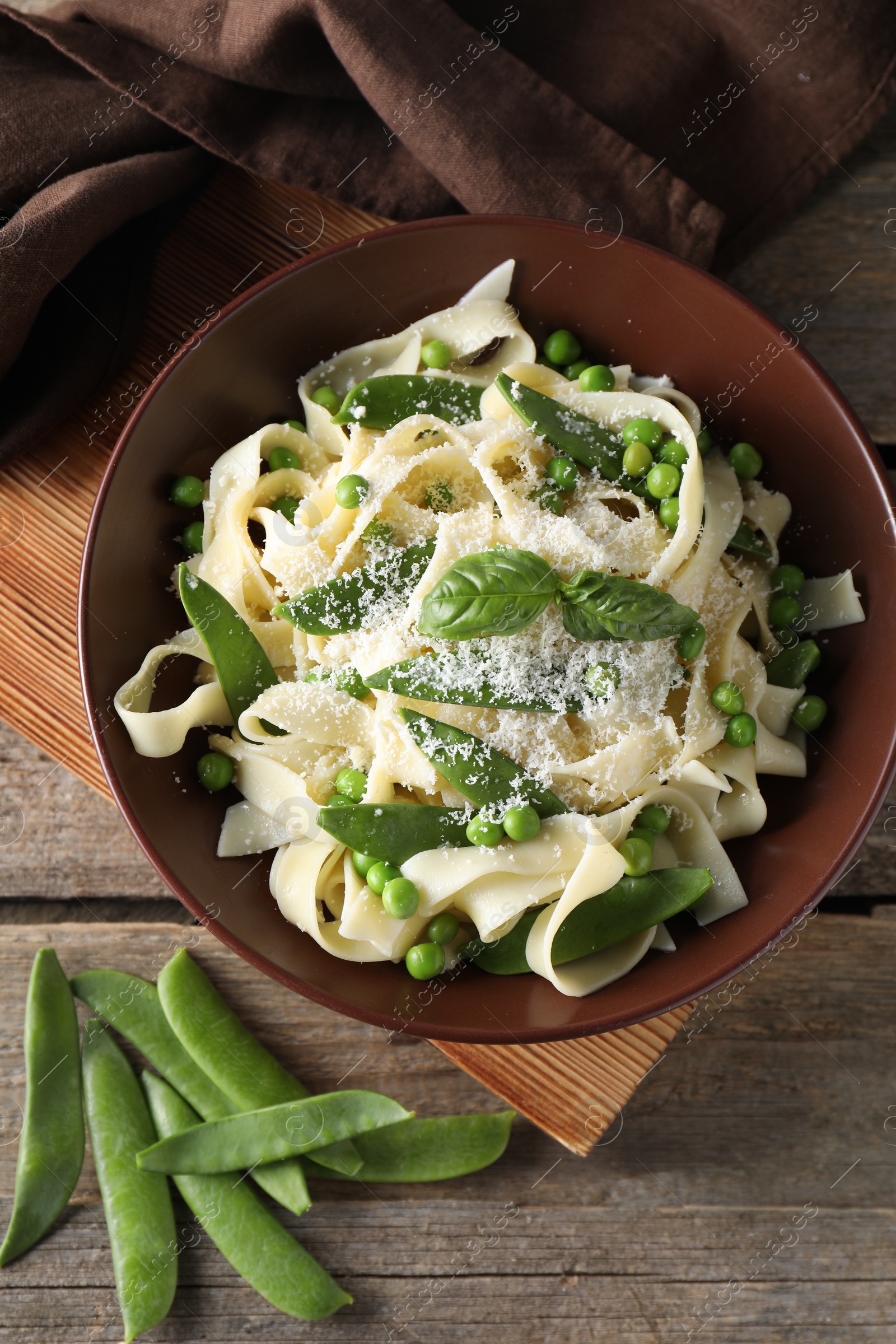 Photo of Delicious pasta with green peas, fresh basil and cheese on wooden table, flat lay