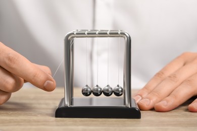 Man playing with Newton's cradle at wooden table, closeup. Physics law of energy conservation