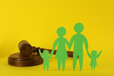 Paper family figure and wooden gavel on yellow background. Child adoption concept