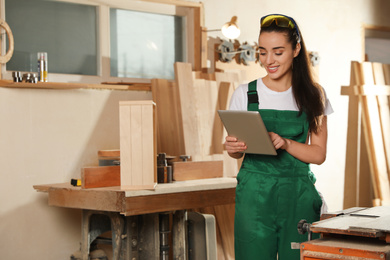 Professional carpenter in uniform with tablet near workbench