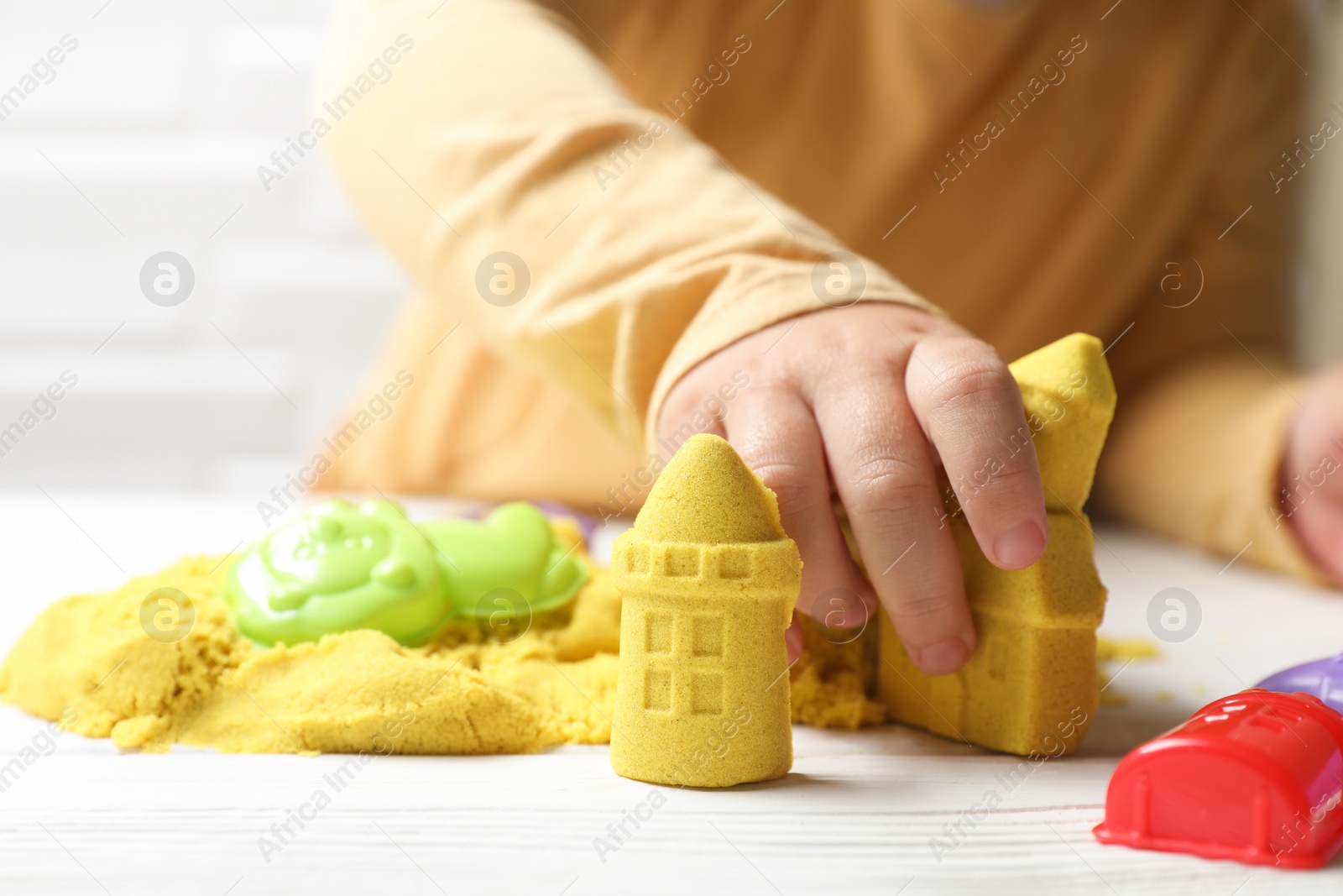 Photo of Little child playing with yellow kinetic sand at white wooden table, closeup