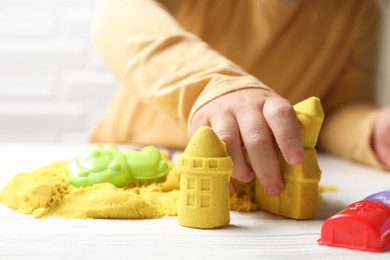 Little child playing with yellow kinetic sand at white wooden table, closeup