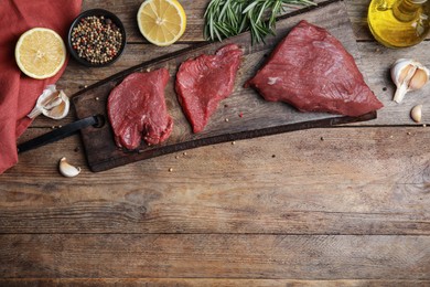 Fresh raw meat steaks and spices on wooden table, flat lay. Space for text
