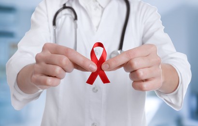 Image of Cancer awareness. Doctor holding red ribbon on blurred background, closeup