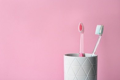 Photo of Cup with toothbrushes against color background