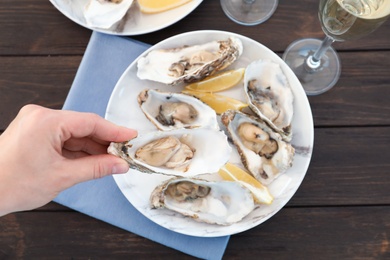 Top view of woman with fresh oyster over plate, focus on hand