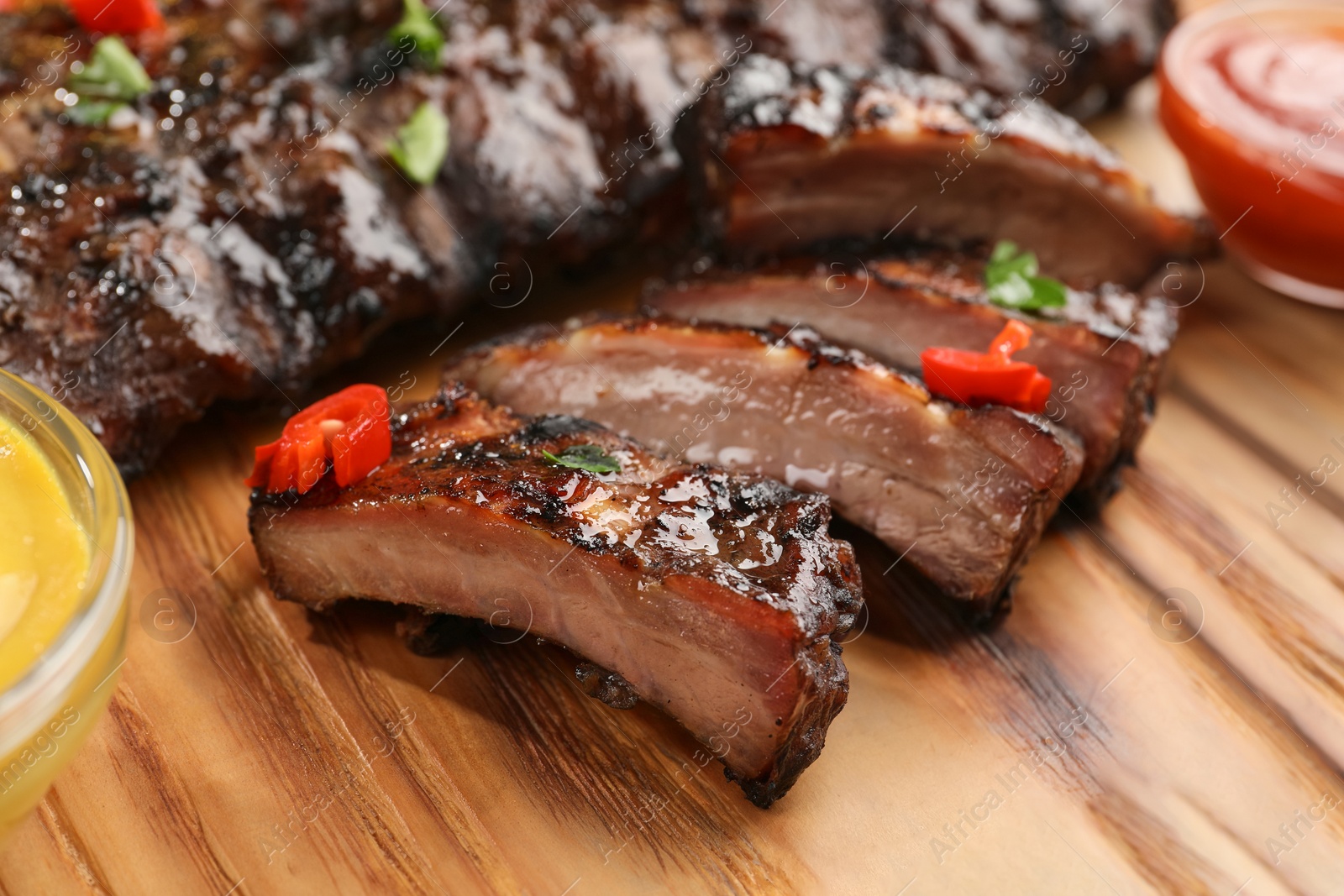 Photo of Tasty grilled ribs and sauce on wooden table, closeup