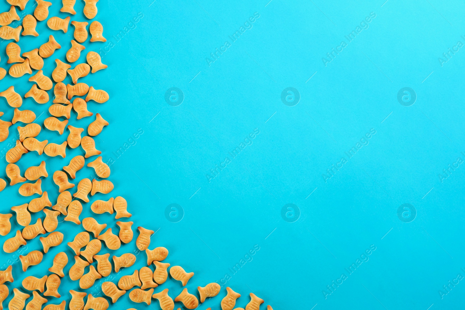 Photo of Delicious goldfish crackers on blue background, flat lay. Space for text