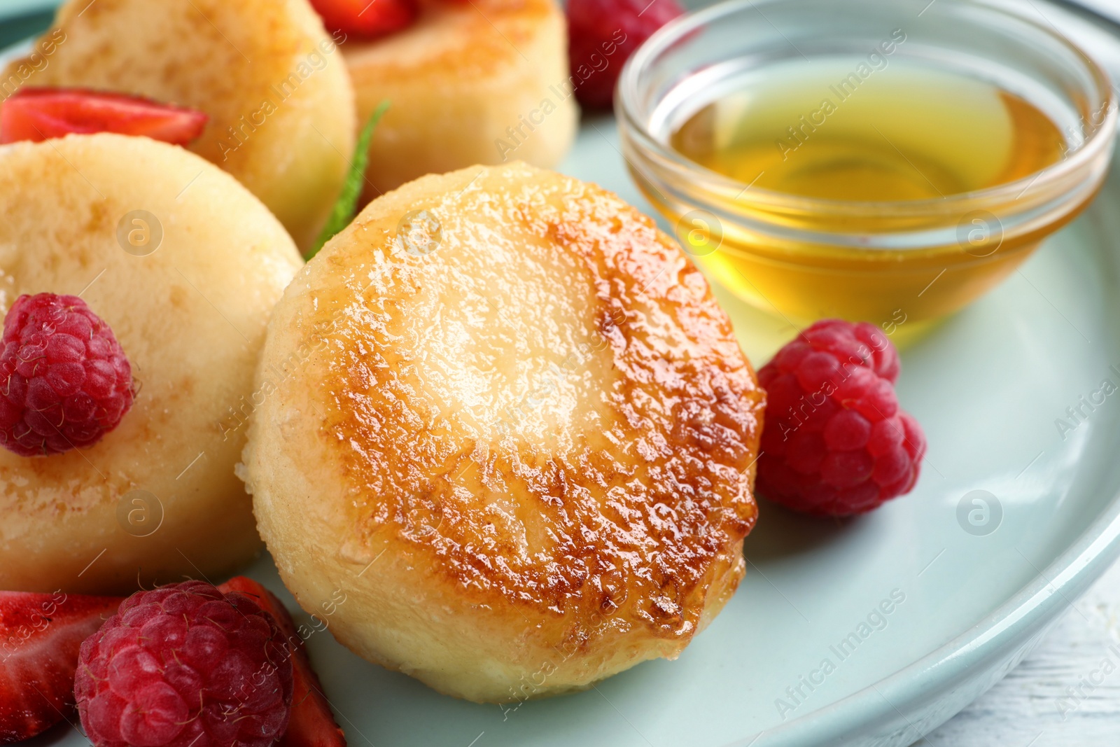 Photo of Delicious cottage cheese pancakes with fresh berries and honey on plate, closeup