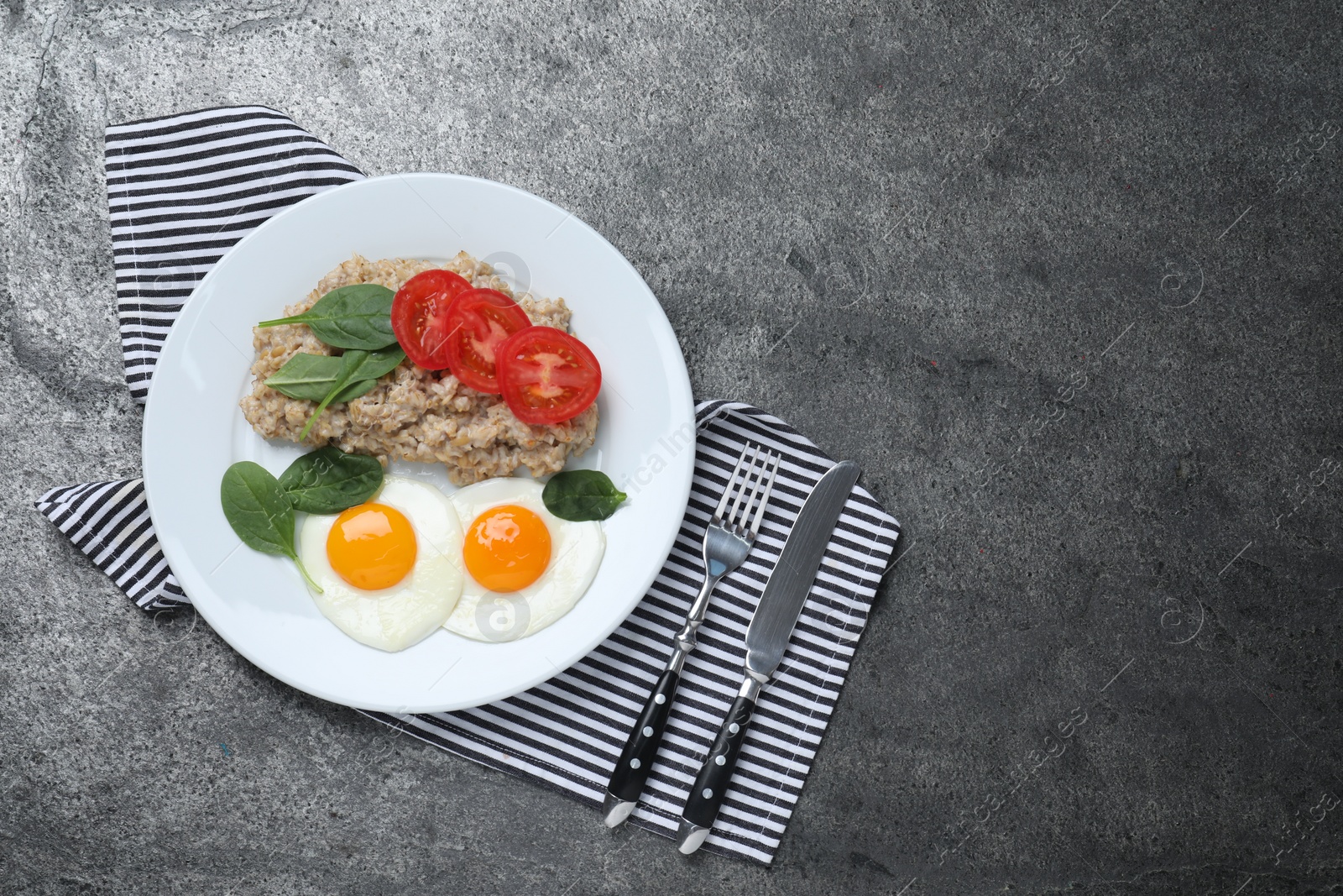 Photo of Delicious boiled oatmeal with fried eggs, tomato and basil served on grey table, flat lay. Space for text