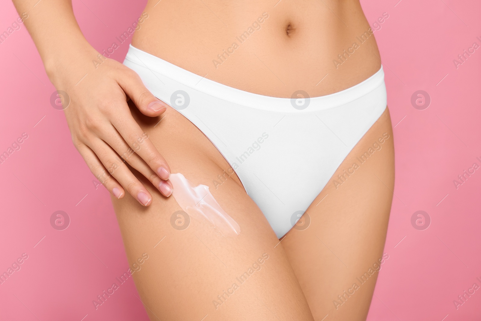 Photo of Young woman applying body cream on leg against pink background, closeup