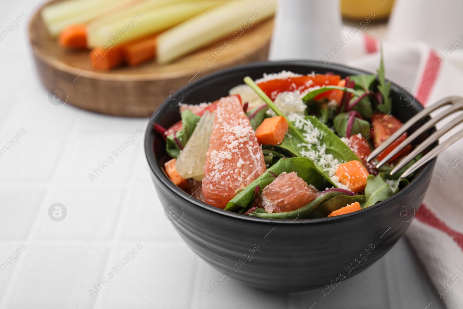 Photo of Delicious salad with pomelo, tomatoes and cheese on white tiled table, space for text