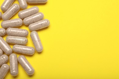 Photo of Many gelatin capsules on yellow background, flat lay. Space for text