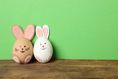 Eggs as cute bunnies on wooden table against green background, space for text. Easter celebration