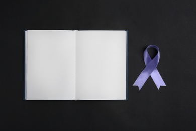Photo of Purple awareness ribbon and open notebook on black background, top view with space for text