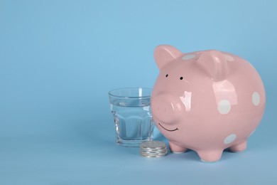 Water scarcity concept. Piggy bank, coins and glass of drink on light blue background, space for text