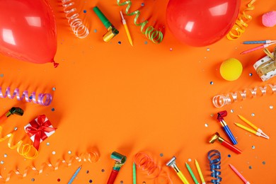 Photo of Frame of colorful serpentine streamers and other party accessories on orange background, flat lay. Space for text