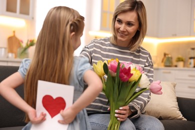 Little girl hiding greeting card for mom at home, selective focus. Happy Mother's Day