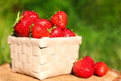 Photo of Basket and ripe strawberries on tree stump outdoors, closeup