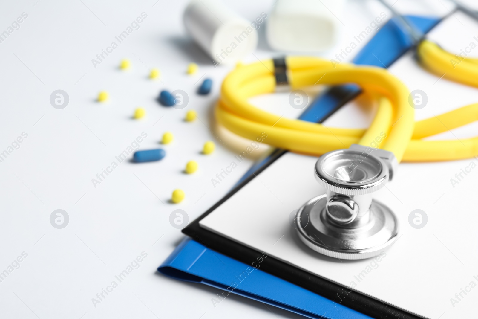 Photo of Stethoscope, clipboard and pills on light background, closeup. Medical equipment