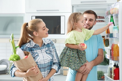 Photo of Happy family with products near refrigerator in kitchen