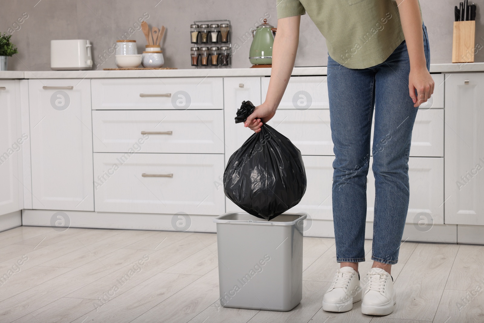 Photo of Woman taking garbage bag out of trash bin in kitchen, closeup. Space for text